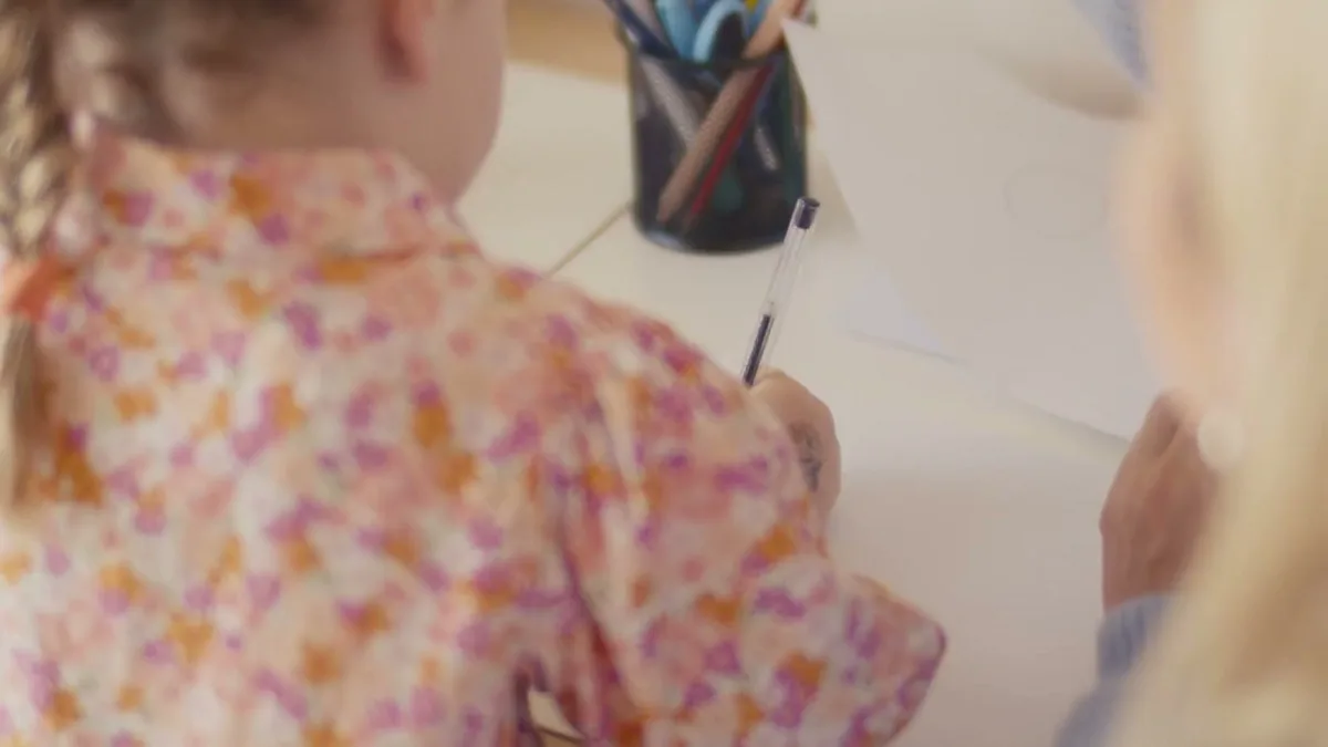 A child drawing at the table while Hayley follows their lead